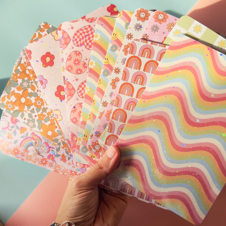 Puede incluir: Un conjunto de 10 hojas de papel de colores con patrones y detalles de purpurina. Los patrones incluyen arco&iacute;ris, corazones, flores y l&iacute;neas onduladas. Las hojas son perfectas para scrapbooking, creaci&oacute;n de tarjetas y otros proyectos de manualidades.