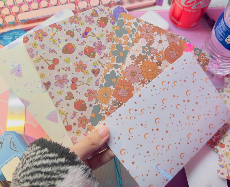 Puede incluir: Cinco hojas de papel decorativo con diferentes patrones. Los patrones incluyen fresas, cerezas, flores y estrellas. El papel es blanco con acentos rosas, naranjas y marrones.