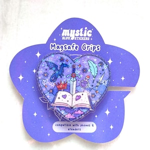 Puede incluir: Un soporte Magsafe morado y azul con un diseño en forma de corazón con temática de fantasía. El diseño incluye un dragón, una espada, una corona, una botella de poción y un libro abierto. El texto "mystic" y "Magsafe Grips" son visibles.