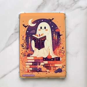 May include: A clear case featuring a Halloween-themed illustration. A friendly ghost reads a book atop a stack of books, with a night sky background, bats, and candles. The case has the text "mysticbluustickers".