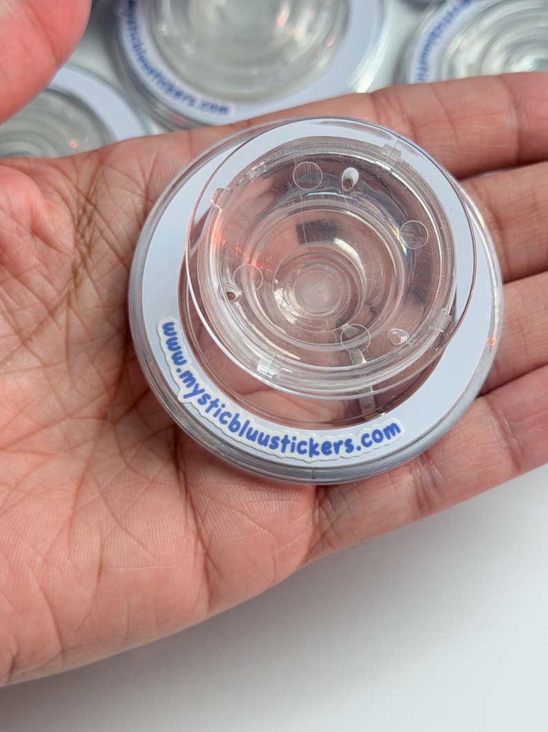 Pu&ograve; includere: Primo piano di adesivi circolari in plastica trasparente con bordo bianco e la scritta "www.mysticbluustickers.com". Gli adesivi hanno un centro trasparente e scanalato.