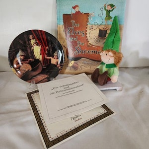 May include: A set of The Elves and the Shoemaker items, including a book, a ceramic plate, a plush elf doll, and a certificate of authenticity. The plate features a colorful illustration of a shoemaker and elves working in a workshop. The book has a colorful cover with an illustration of elves making shoes. The plush elf doll is wearing a green hat and a green and brown outfit. The certificate of authenticity is framed in gold and has the text "Der Schuhmacher und die Heinzelmännchen" printed on it.