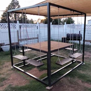 May include: A black metal swing set with a wooden table and four swings. The swing set is in a backyard with a white fence and green grass.