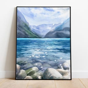 May include: Watercolor painting of a mountain lake with a rocky shore. The water is a light blue color and the mountains are a dark blue color. The sky is a light blue color with white clouds.