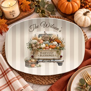 May include: An oval serving platter featuring a vintage truck illustration filled with pumpkins, flowers, and greenery. The text reads The Wilson's, Pumpkin Patch, Harvest Blessings, and Autumn. The background has vertical beige and white stripes.