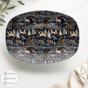 May include: An oval serving platter with a dark blue background featuring a repeating pattern of deer, trees, and foliage in gold, white, and gray. The platter is labeled as dishwasher, microwave, and oven safe.