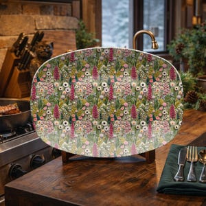 Puede incluir: Una fuente ovalada para servir con un estampado floral. El diseño presenta una variedad de flores en tonos rosa, blanco y amarillo sobre un fondo verde. La fuente se exhibe sobre un soporte de madera, lo que sugiere su uso para servir alimentos.