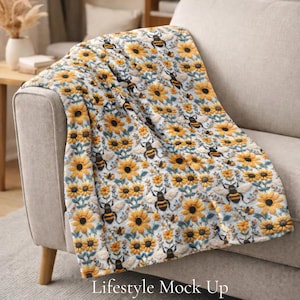 May include: A soft, light blue blanket with a pattern of yellow sunflowers and black and yellow bees. The blanket is draped over a beige sofa. The text "Lifestyle Mock Up" is at the bottom of the image.