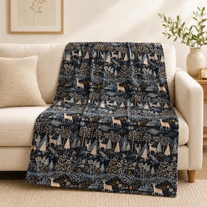 May include: A dark navy blue throw blanket featuring a repeating pattern of white and gold deer, stylized evergreen trees, and floral elements. The design includes intricate details of woodland creatures and forest foliage across the fabric surface.