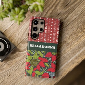 May include: A phone case with a floral design and the word "BELLADONNA" printed on it. The case features a red and green floral pattern with a tribal design on the top. The phone case is on a wooden surface.