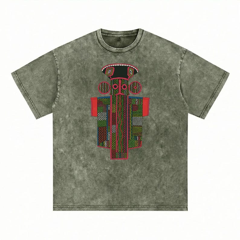 K&ouml;nnte beinhalten: Ein kurz&auml;rmeliges T-Shirt in verwaschenem Olivgr&uuml;n mit Mineral-Wash-Optik. In der Mitte befindet sich eine Grafik einer stilisierten, symmetrischen Figur mit breitem Hut, kreisf&ouml;rmigen Ohren und einem rechteckigen K&ouml;rper mit komplexen Mustern.