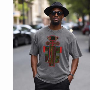 K&ouml;nnte beinhalten: Ein anthrazitfarbenes Kurzarm-T-Shirt mit einem zentralen Grafikdruck einer stilisierten, symmetrischen Figur mit komplexen geometrischen Mustern in Rot, Gr&uuml;n, Gelb und Schwarz. Das T-Shirt hat einen Rundhalsausschnitt und eine verwaschene Textur.