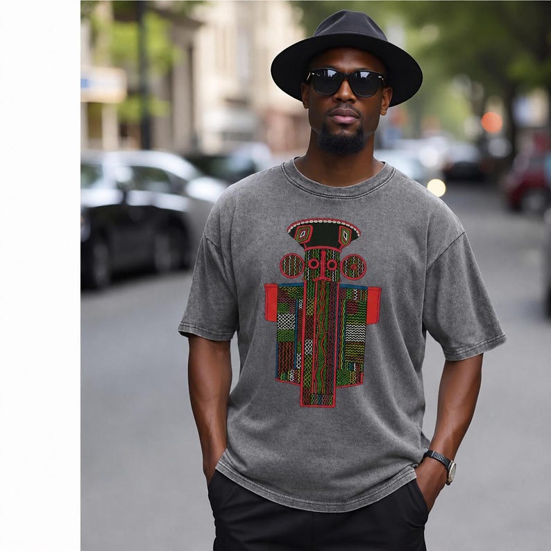 K&ouml;nnte beinhalten: Ein anthrazitfarbenes Kurzarm-T-Shirt mit einem zentralen Grafikdruck einer stilisierten, symmetrischen Figur mit komplexen geometrischen Mustern in Rot, Gr&uuml;n, Gelb und Schwarz. Das T-Shirt hat einen Rundhalsausschnitt und eine verwaschene Textur.