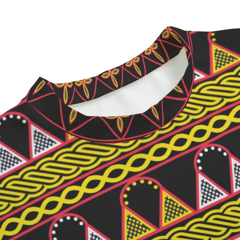 May include: Close-up of a black crew neck shirt with a vibrant, repeating pattern. The design features yellow, red, and white geometric shapes and lines. The collar is white.