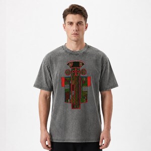 K&ouml;nnte beinhalten: Ein anthrazitfarbenes T-Shirt in Acid-Wash-Optik mit einem zentralen Grafikdesign. Der Druck zeigt eine stilisierte, symmetrische Figur mit einem geometrischen Muster in Rot, Gr&uuml;n und Schwarz, akzentuiert durch wei&szlig;e Punkte und eine rote Basis.