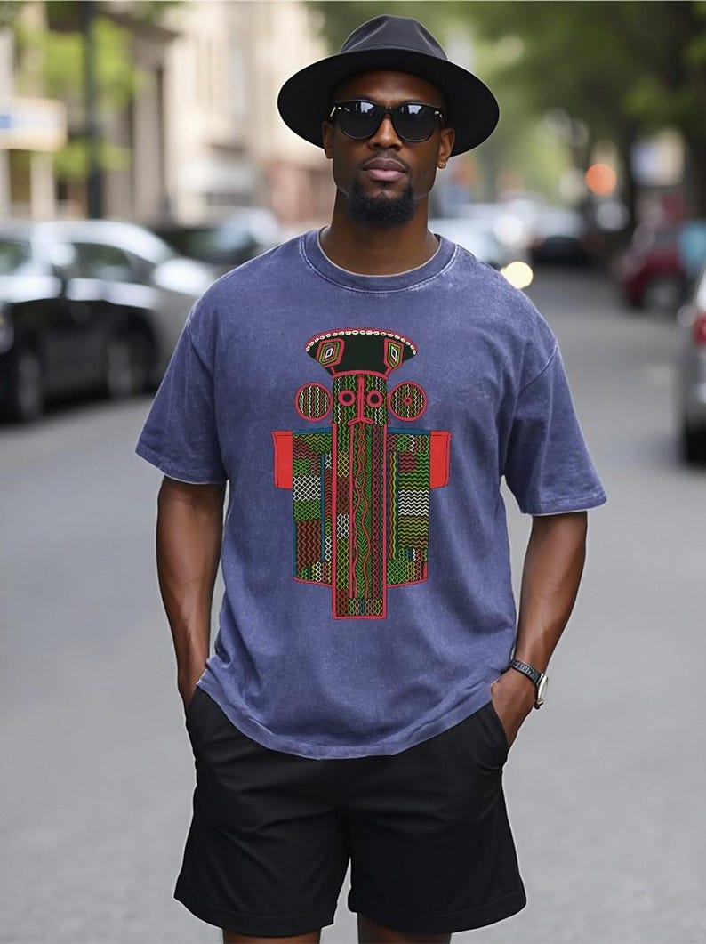 K&ouml;nnte beinhalten: Ein blaues kurz&auml;rmeliges T-Shirt mit einem zentralen Grafikdruck mit geometrischen Mustern in Rot, Gr&uuml;n und Gelb. Das Design zeigt eine stilisierte Figur mit kreisf&ouml;rmigen Elementen und einem flachen Oberteil auf verwaschenem blauem Stoff.