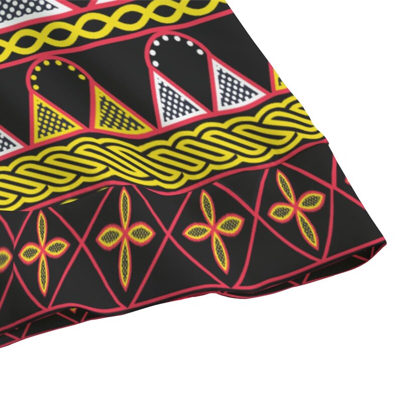 May include: Close-up of a black fabric with a repeating pattern. The design features yellow, red, and white geometric shapes, including triangles, diamonds, and floral motifs. The edges are trimmed with a red border.
