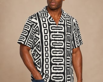May include: A short-sleeved button-down shirt featuring a bold black and white geometric pattern with vertical stripes, triangular motifs, and square outlines. The shirt has a classic collar, a buttoned front placket, and a straight hemline.