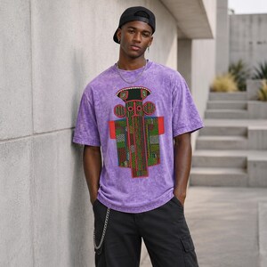K&ouml;nnte beinhalten: Ein violettes Acid-Wash-T-Shirt mit einer zentralen Grafik einer stilisierten Figur mit geometrischen Mustern in Rot, Gr&uuml;n und Schwarz. Dazu werden eine schwarze Baseballkappe, eine silberne Halskette und eine schwarze Cargohose mit Kette getragen.