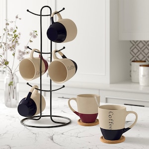 May include: A set of six ceramic coffee mugs with black and burgundy accents. The mugs are displayed on a black metal mug tree. The mugs have the word "Coffee" written on them.
