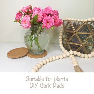 May include: Two cork pads, one on top of the other, with a small glass vase filled with pink roses on top. A white wooden bead garland is in the foreground. The text "Suitable for plants DIY Cork Pads" is at the bottom of the image.
