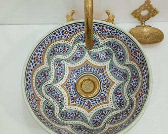 May include: A white ceramic sink with a blue, green, and red geometric pattern. The sink has a gold-colored drain and a gold-colored faucet.