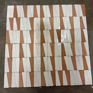 以下が含まれることがあります： 幾何学模様に配置された、テラコッタと白のセラミックタイル48枚セット。タイルは長方形で、白い斜めストライプが入っています。