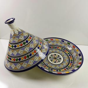 May include: A ceramic tagine, a traditional North African cooking vessel, with a conical lid and a matching base. The tagine features a vibrant, geometric pattern in blue, yellow, red, and green. The base is round with a similar design.
