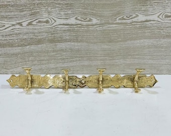 May include: A brass wall-mounted coat rack with four hooks. The rack has an ornate, decorative design with floral and scrollwork patterns. The hooks are evenly spaced along the rack, which is approximately 18 inches long.