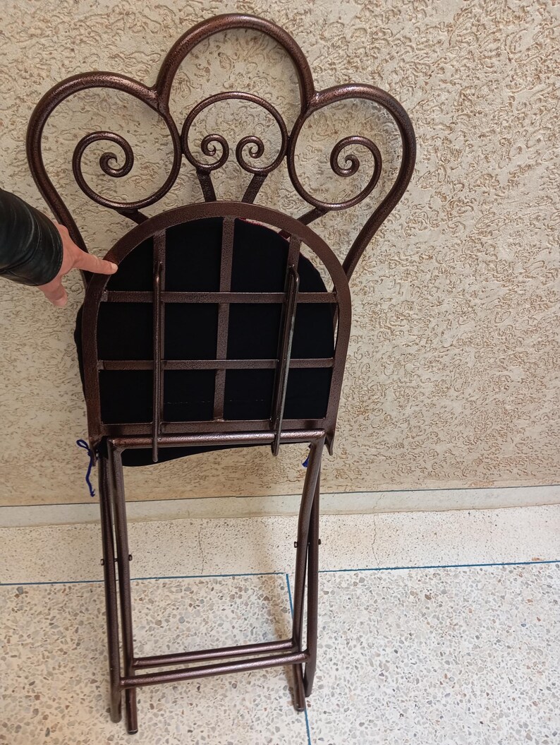 Op de afbeelding: Een bruine metalen vouwstoel met een zwarte stoffen zitting en een decoratieve, gerolde rugleuning.