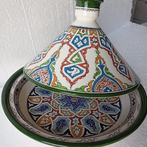 May include: A ceramic tagine pot with a conical lid and a round base. The lid and base feature colourful geometric patterns in blue, red, orange, and green against a white background. The rim and lid top are green.