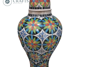 May include: A large, white ceramic vase with a lid. The vase is decorated with a colorful geometric pattern of blue, green, red, yellow, and black. The lid has a similar pattern.