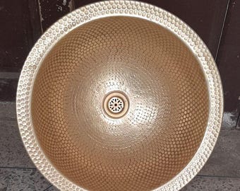 May include: A gold-colored, round, hammered metal sink with a drain in the center.