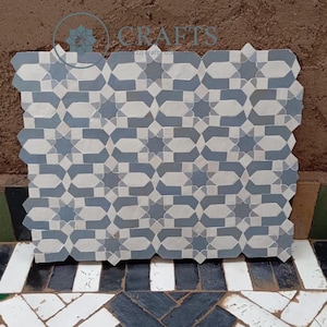 May include: A geometric tile design in shades of blue and white. The pattern features interlocking shapes and stars, creating a visually appealing mosaic. The tile is displayed on a textured brown surface, showcasing the craftsmanship.