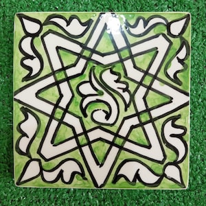 Puede incluir: Un azulejo de cerámica verde y blanco con un diseño geométrico en blanco y negro. El diseño presenta una forma de estrella con líneas y curvas intrincadas.