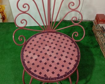 Op de afbeelding: Een decoratieve roze metalen stoel met een mozaïektegelzitting. De rugleuning van de stoel heeft een waaiervormig ontwerp met kruldetails. De ronde zitting heeft een dambordpatroon. De stoel heeft gebogen poten.