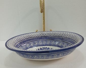 May include: A white ceramic oval sink with a blue and white geometric pattern. The sink has a gold metal faucet with a decorative design.