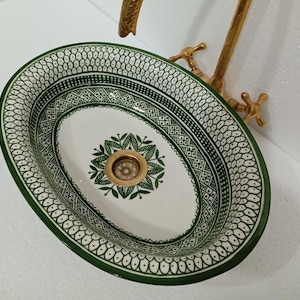 Pode incluir: Pia de cerâmica oval com um padrão geométrico verde e branco. A pia tem um ralo no centro e é projetada para um banheiro.