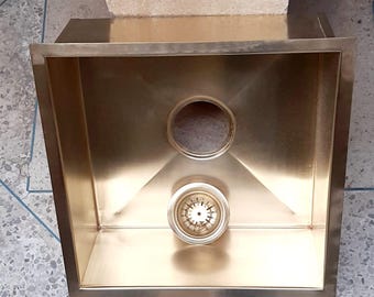 Puede incluir: Un fregadero de cocina de acero inoxidable de color dorado con un desagüe redondo y un colador.