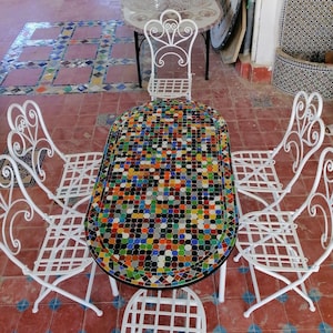 Pode incluir: Conjunto de móveis de pátio de metal branco com uma mesa redonda de mosaico. O tampo da mesa é feito de azulejos coloridos em uma variedade de formas e tamanhos.