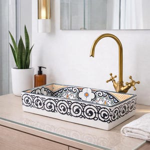 Op de afbeelding: Rechthoekige keramische badkamer wastafel met een decoratief zwart-wit wervelpatroon. De wastafel heeft een kleurrijk interieurontwerp en is gecombineerd met een gouden kraan. Een witte handdoek ligt op het aanrecht.