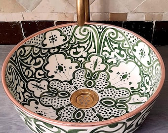 Puede incluir: Un lavabo de cerámica blanca con un diseño floral verde y negro. El lavabo tiene un borde de cobre y un desagüe de oro.