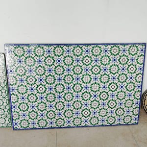 May include: Rectangular tile panels with a repeating geometric pattern in white, green, and blue. The tiles have a blue border. The design features star-like shapes, creating a visually appealing and intricate mosaic.