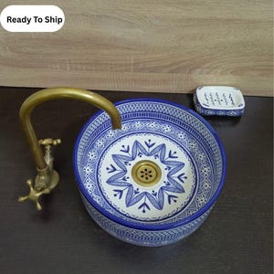 May include: A round, blue and white ceramic sink with a decorative floral pattern. A brass faucet is attached to the sink. A matching soap dish is also present. The sink is a decorative bathroom fixture.