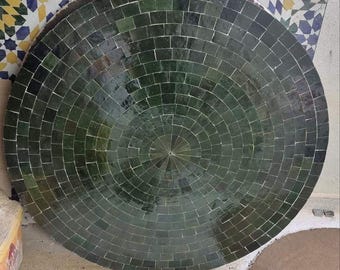 Puede incluir: Una gran mesa redonda hecha de azulejos verdes oscuros dispuestos en un patrón concéntrico. Los azulejos son cuadrados y crean una superficie texturizada. La mesa tiene aproximadamente 122 cm de diámetro, adecuada para uso en exteriores o interiores.