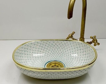 May include: A decorative ceramic sink with a gold rim and a gold faucet. The sink has a white background with a blue and white pattern. The faucet is a curved design with two handles.