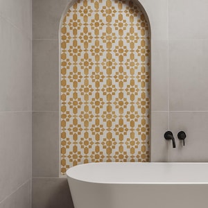 Puede incluir: Un baño moderno con bañera blanca y paredes de azulejos grises. Una alcoba arqueada presenta un patrón de azulejos decorativo en oro y blanco. Grifos negros montados en la pared sobre la bañera.