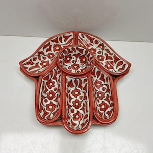 May include: A red and white ceramic serving dish with a floral design. The dish is shaped like a hand with a central round bowl and four surrounding compartments. The floral pattern is red on a white background.