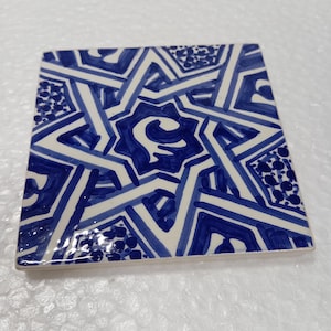 Puede incluir: Un azulejo de cerámica azul y blanco con un patrón geométrico. El azulejo presenta un diseño de estrella con líneas y puntos intrincados.
