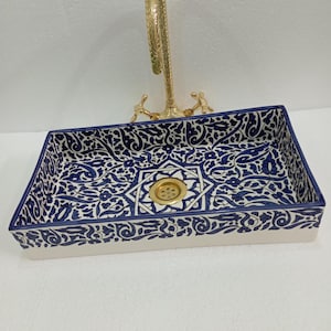 May include: A white ceramic bathroom sink with a blue and white floral pattern. The sink has a round drain and a rectangular shape.